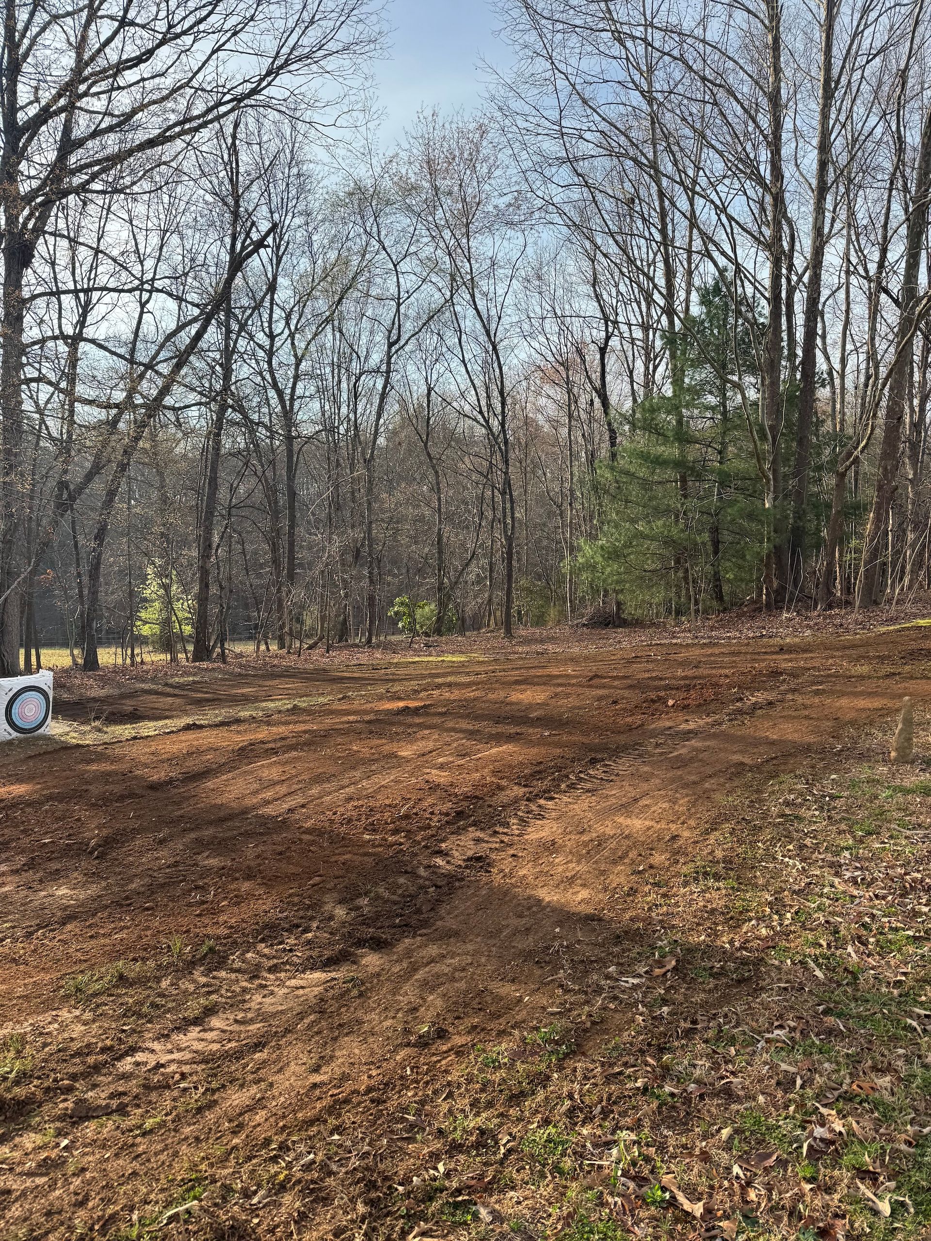 A clearing of tilled brown dirt in a forest with bare trees, with a white target on the left edge.