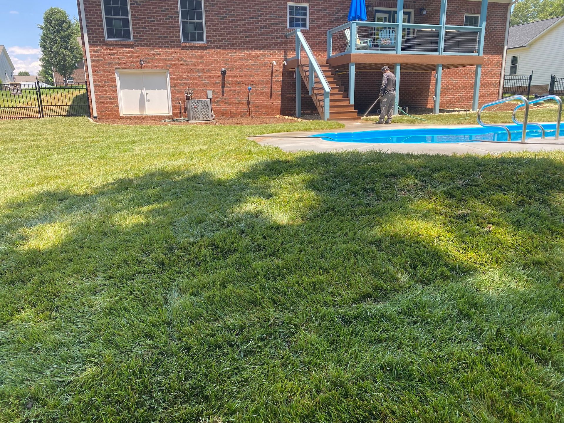 A brick house with a deck and stairs overlooking a backyard with a swimming pool and a person standing near the deck.