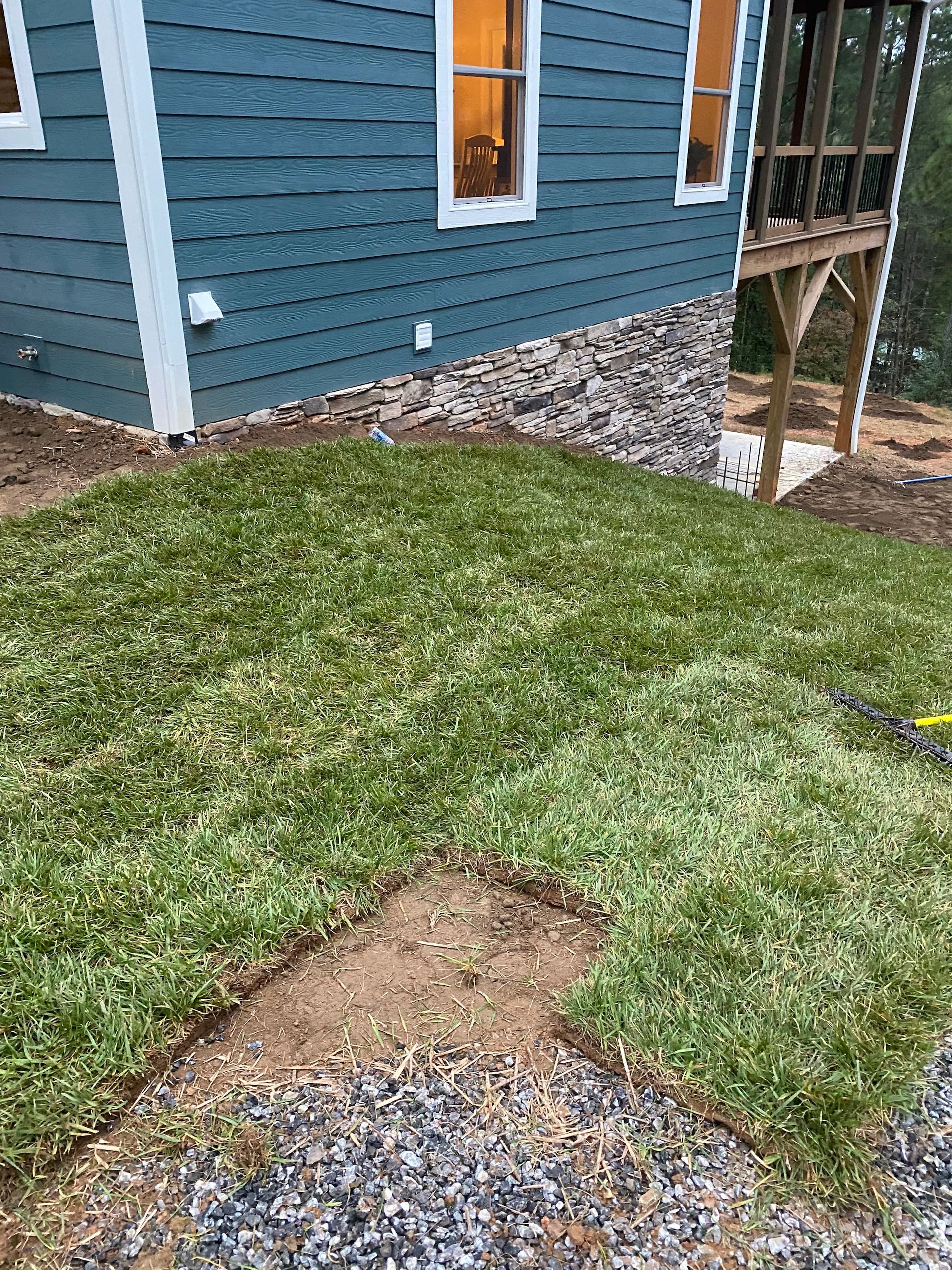 Newly laid sod patches on a sloped lawn next to a blue house with stone foundation trim.