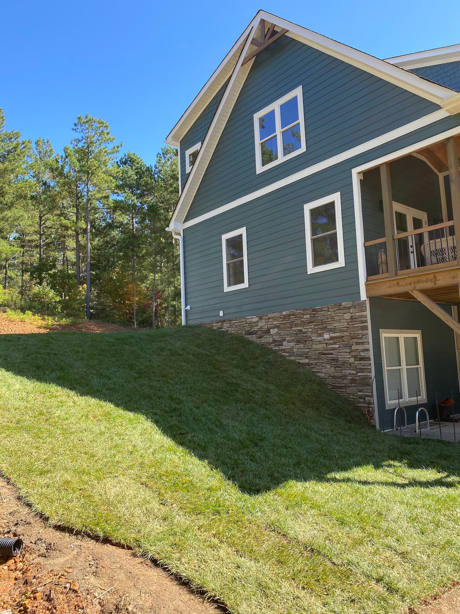 A blue house with a stone foundation and freshly laid sod on a sloped lawn against a clear blue sky.