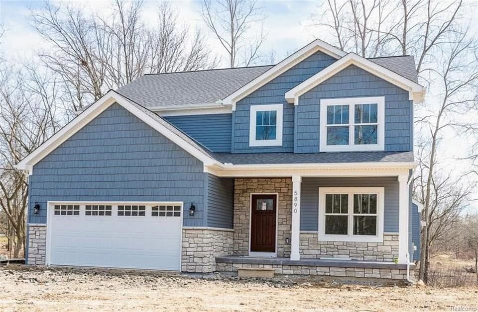 Blue two-story house with white trim, stone accents, and attached garage in a winter setting Blue two-story house with white trim, stone accents, and attached garage in a winter setting