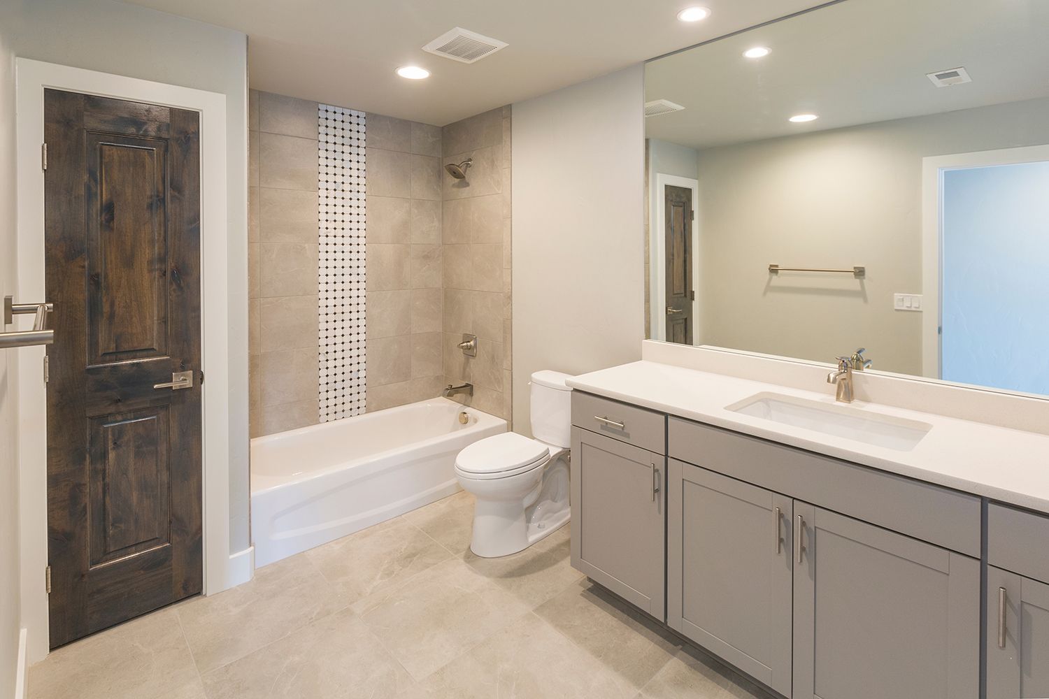 Modern beige bathroom with double vanity, bathtub, toilet, and rustic wooden door Modern beige bathroom with double vanity, bathtub, toilet, and rustic wooden door