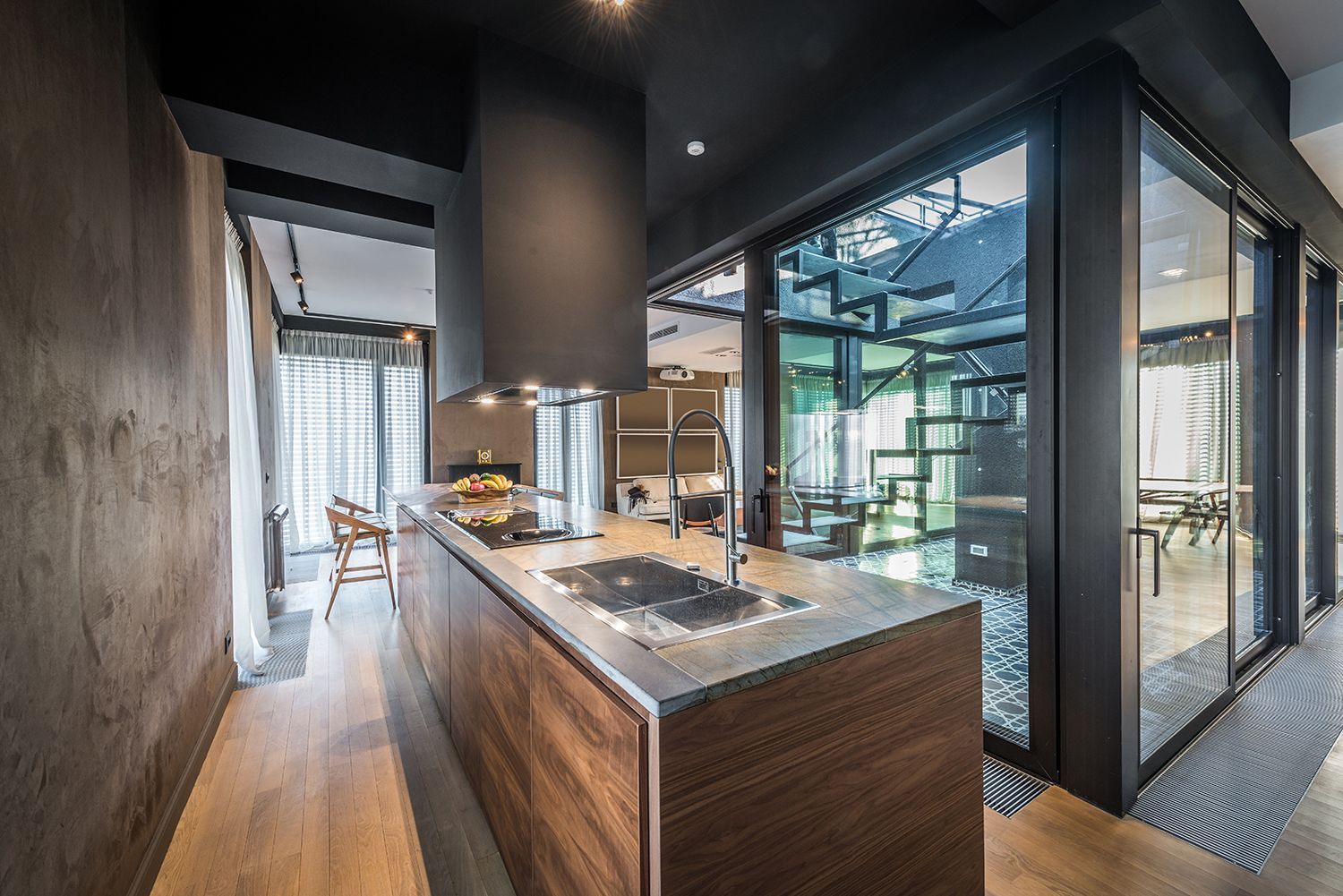 Modern kitchen with wood island, dark walls, and floor-to-ceiling glass overlooking a bright exterior Modern kitchen with wood island, dark walls, and floor-to-ceiling glass overlooking a bright exterior