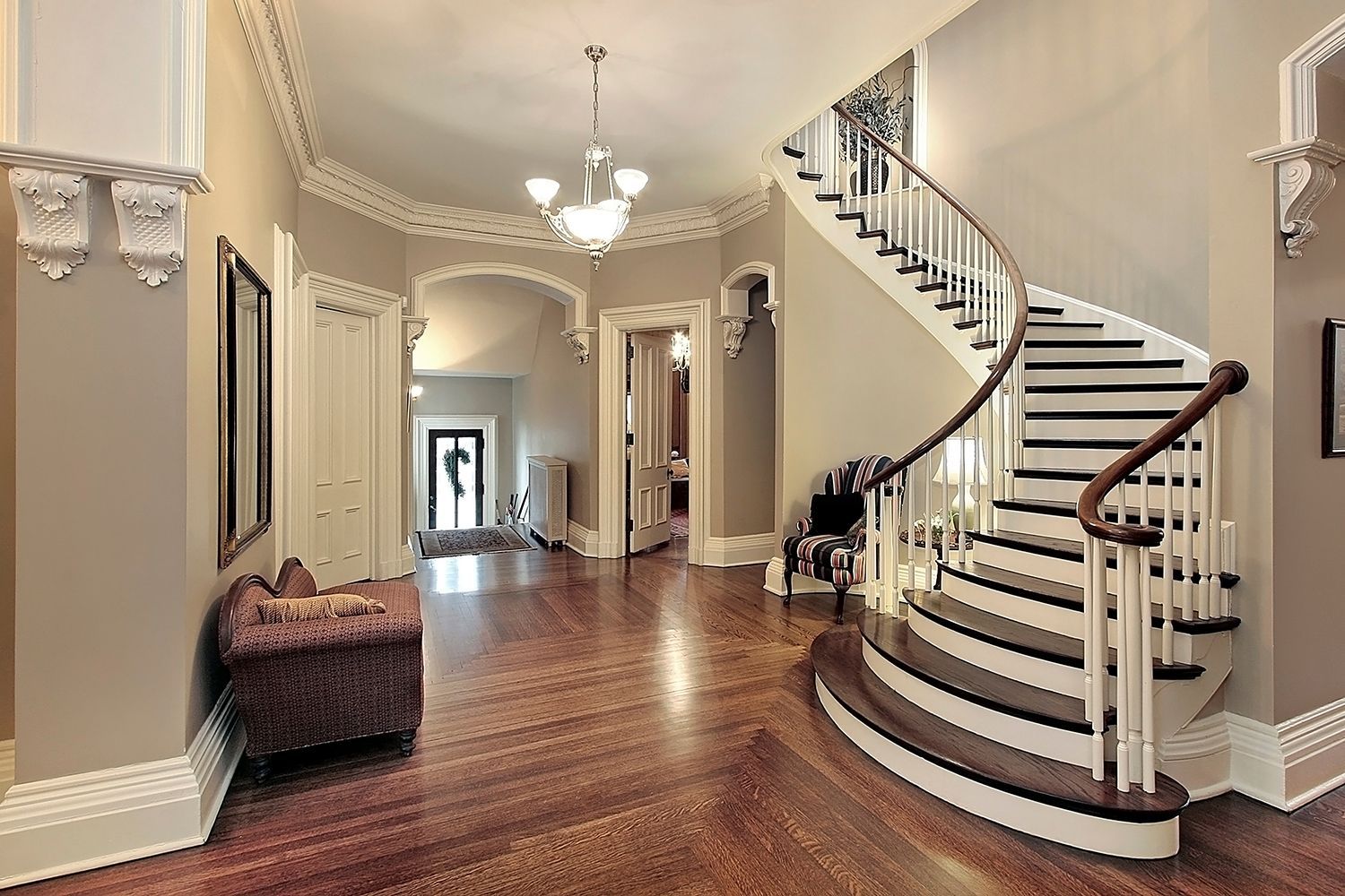 Elegant foyer with curved staircase, hardwood floors, and chandelier in a bright home interior Elegant foyer with curved staircase, hardwood floors, and chandelier in a bright home interior