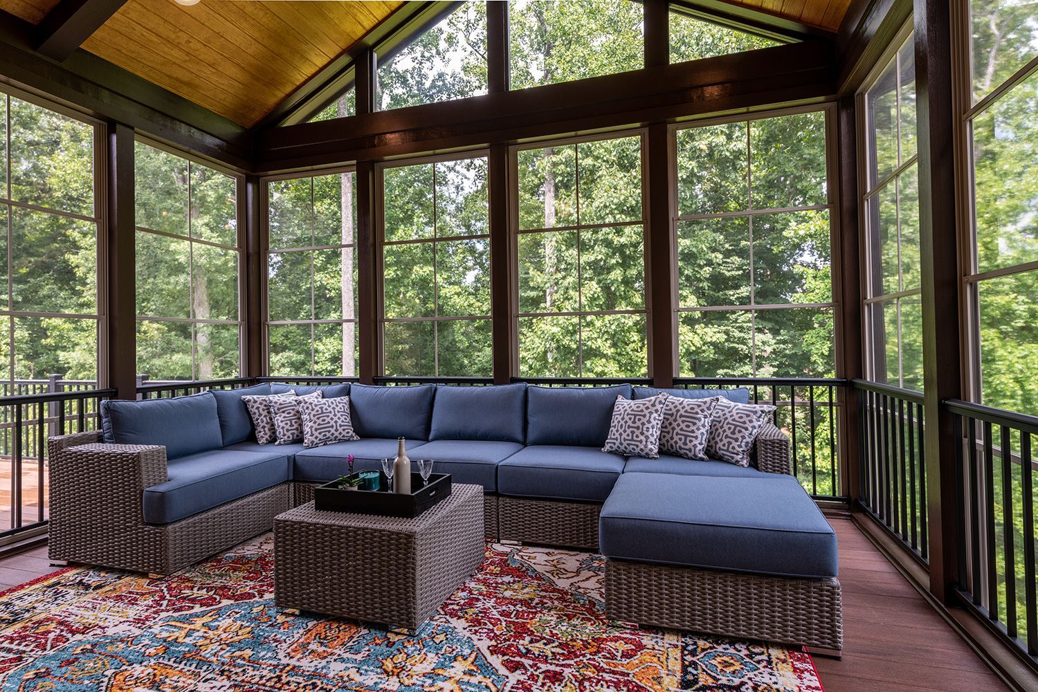 Screened porch with blue sectional sofa, wicker table, and colorful rug overlooking trees Screened porch with blue sectional sofa, wicker table, and colorful rug overlooking trees