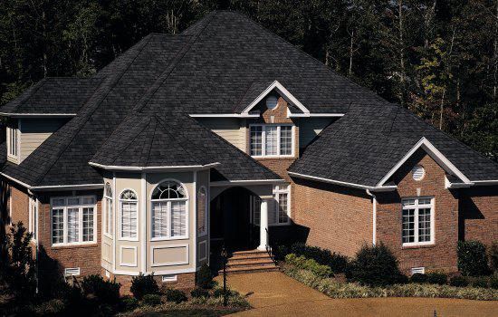 Large brick house with dark roof, white-trimmed windows, and a front porch surrounded by trees