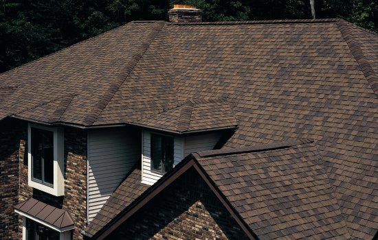 Brown shingled roof of a house, viewed from above with dormer windows.