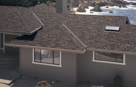 Aerial view of a gray house with a dark shingled roof and multiple windows.