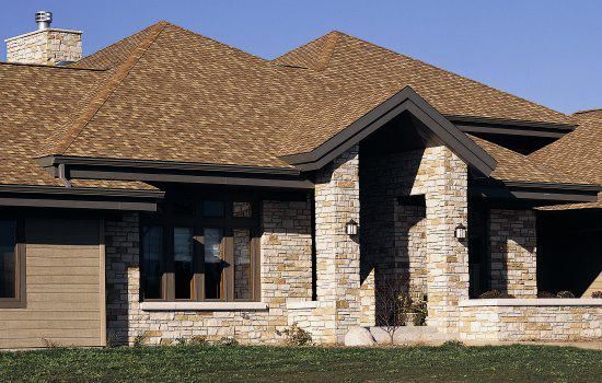 Stone suburban house with tan shingled roof, front windows, and covered porch in daylight