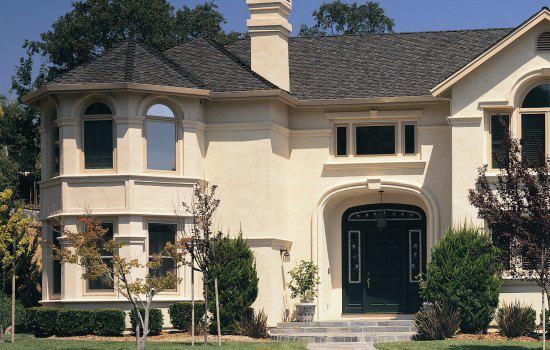 Large cream-colored suburban house with arched entry, bay windows, and a front lawn