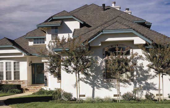Suburban house with a gray roof, white exterior, and small trees in the front yard.