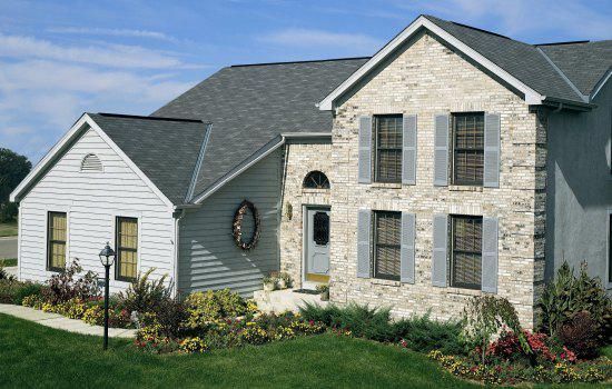 Suburban two-story house with stone facade, gray siding, and landscaped front yard