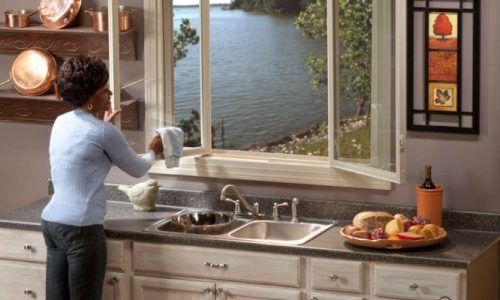 Person at kitchen sink washing dishes beside a bright window overlooking water
