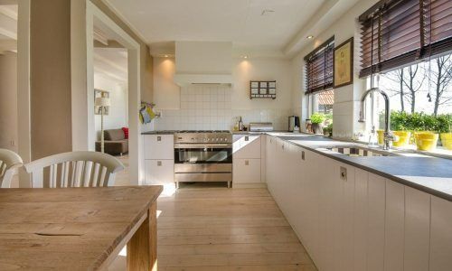 Bright modern kitchen with white cabinets, wooden table, and large window over a long countertop