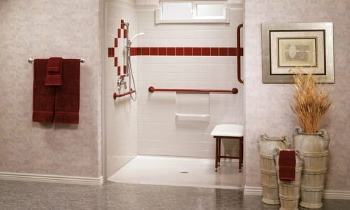 Bathroom with white tub, red towel accents, grab bar, stool, and framed art on a beige wall