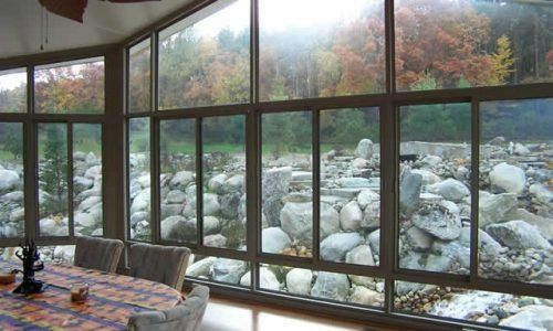 Large windows overlooking a rocky river and autumn trees from a cozy indoor room