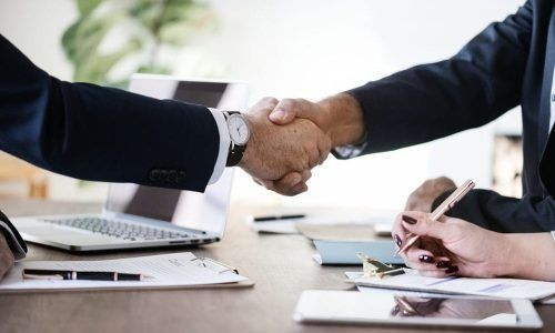 Two businesspeople shaking hands across a desk in a bright office