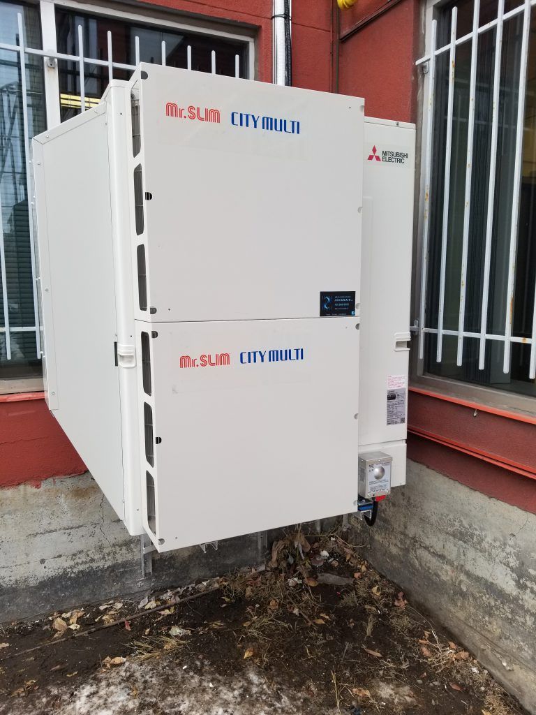 Une grande boîte blanche est suspendue au côté d'un bâtiment.