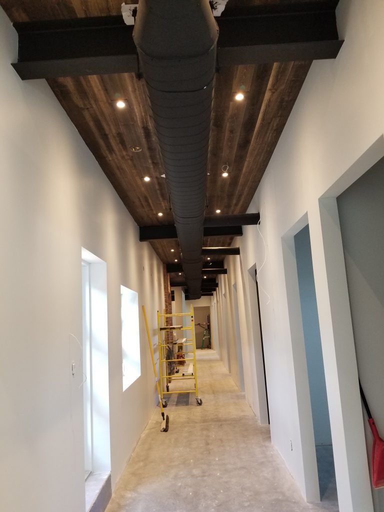 Un long couloir avec un plafond en bois et un tuyau noir suspendu au plafond.