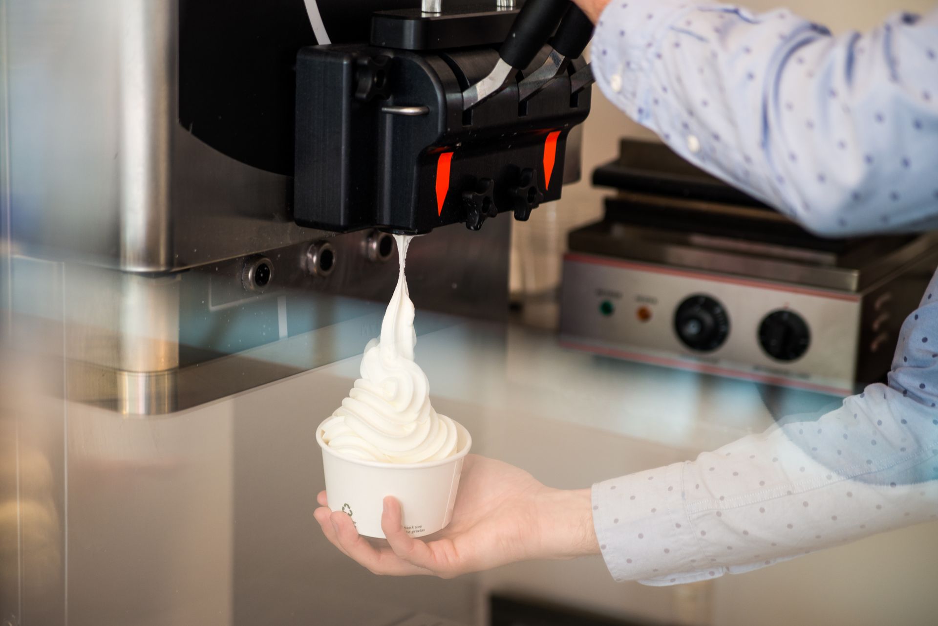 Une machine distribue de la crème glacée molle dans un gobelet, tenu par une personne.