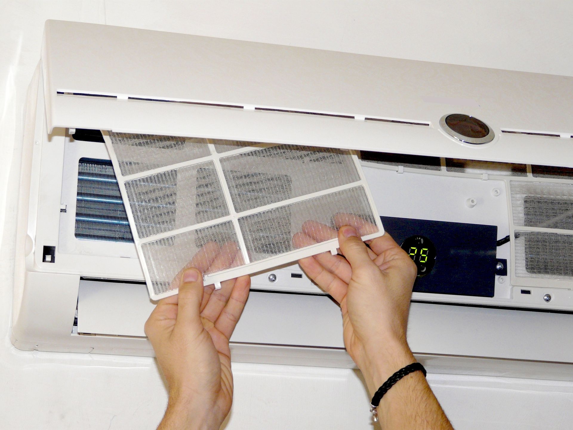 Une personne retire le filtre à air d'un climatiseur blanc fixé au mur.