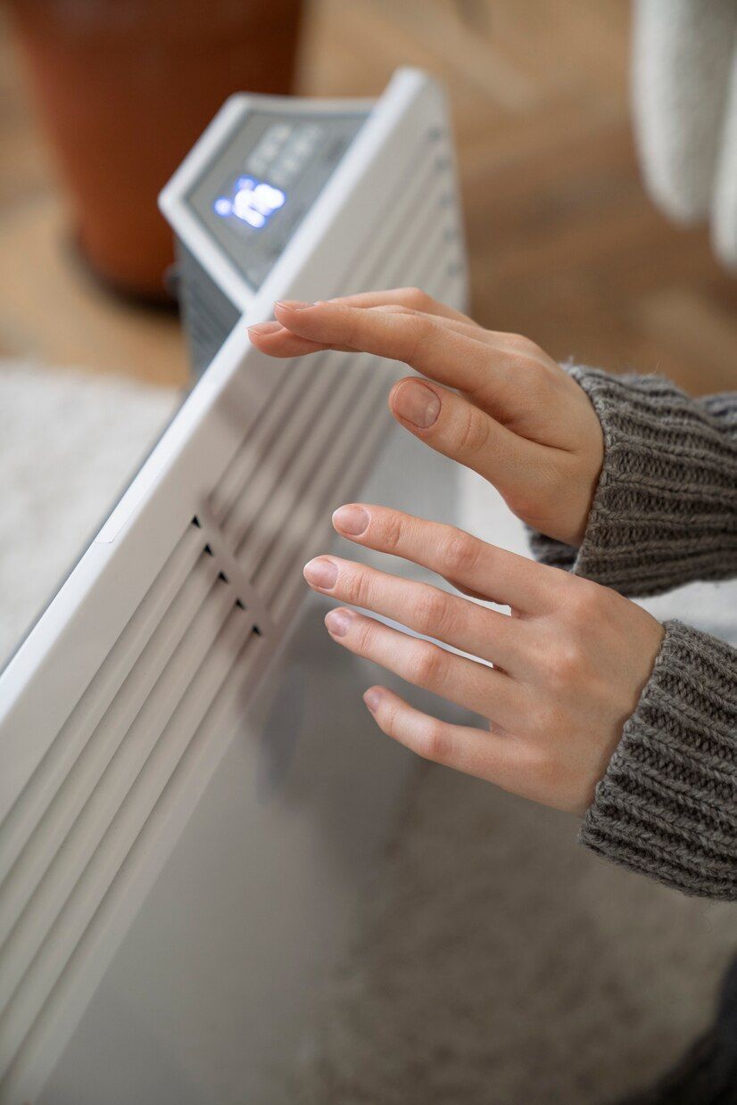 Mains se réchauffant au-dessus d'un radiateur d'appoint blanc à affichage numérique