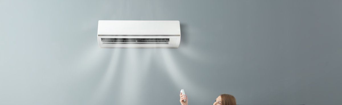 Un climatiseur souffle de l'air froid, une personne tient la télécommande.
