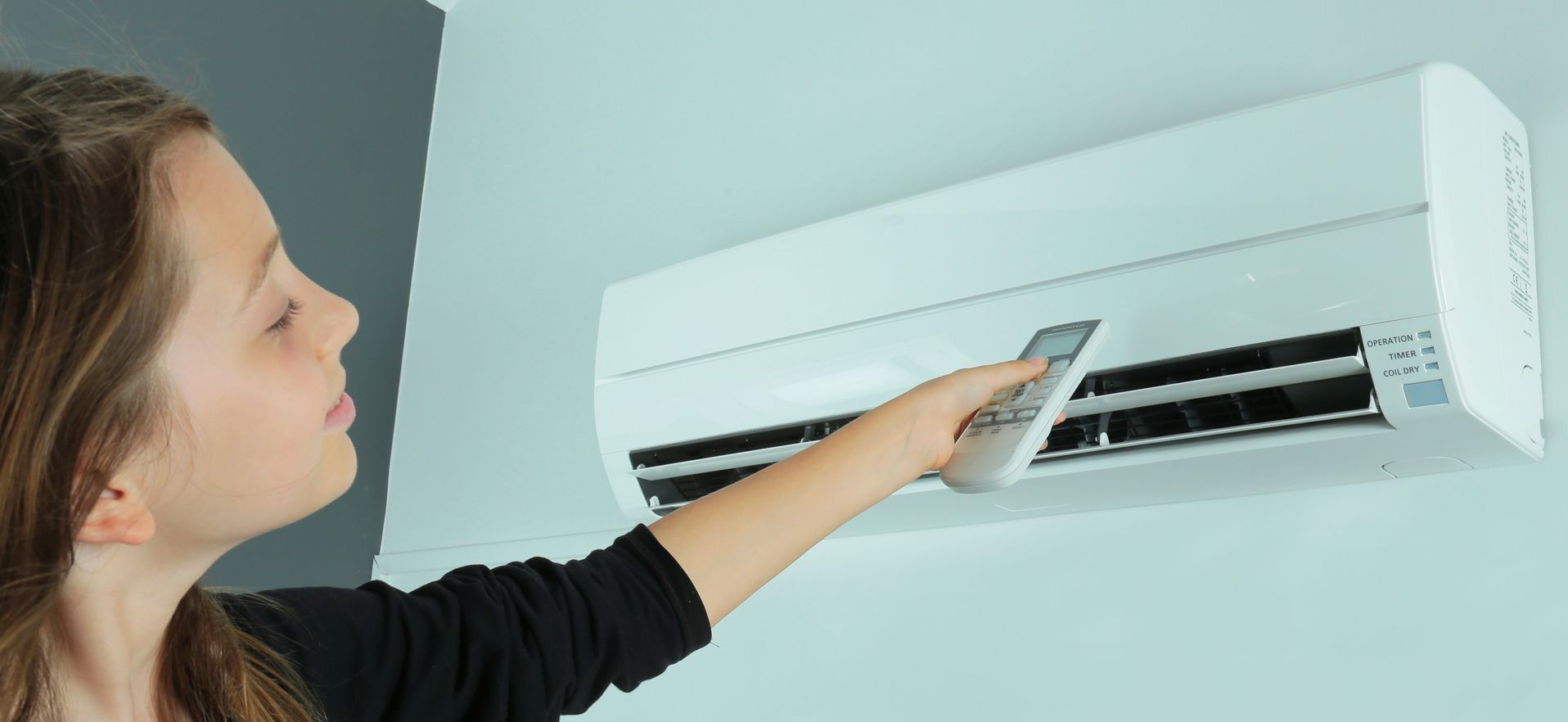 Une personne utilise une télécommande pour commander un climatiseur blanc fixé au mur.