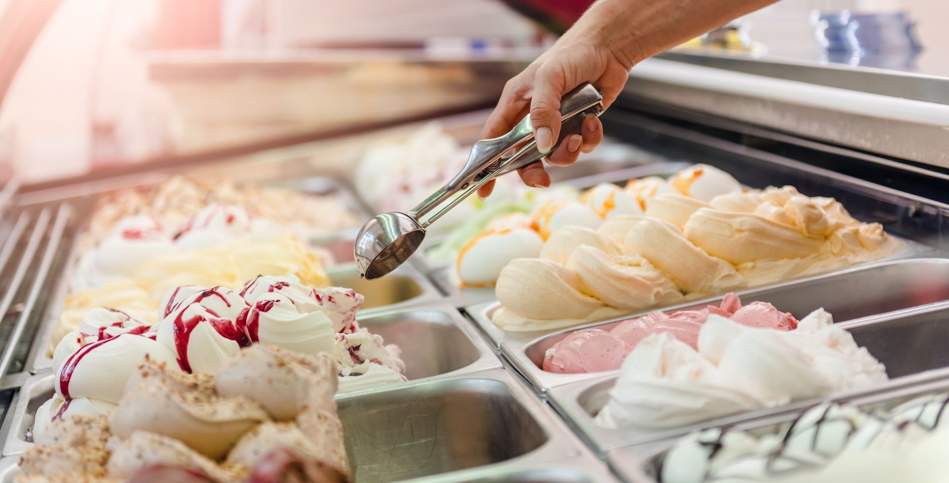 Main versant de la crème glacée à l'aide d'une cuillère dans des bacs de réfrigération commerciale.