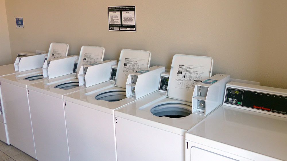 Row of white top-loading washing machines in a laundromat with a detergent dispenser on the right