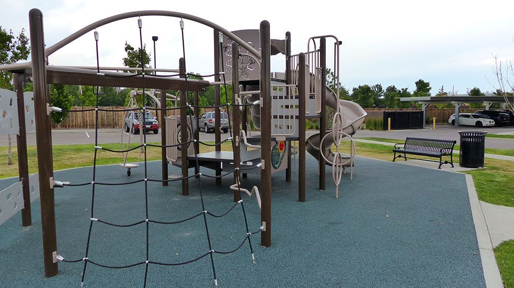 Playground climbing structure with rope net, slides, and benches in a park under a cloudy sky