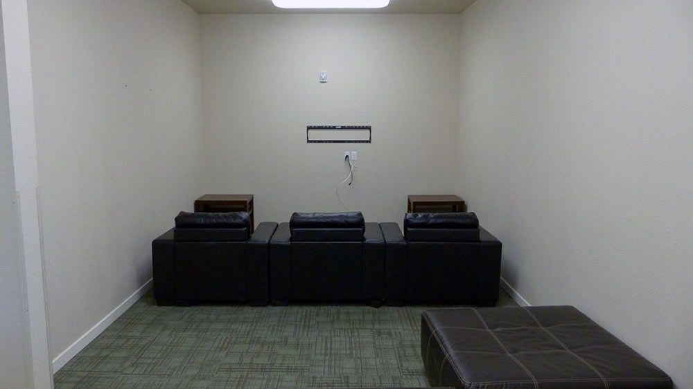 Empty room with beige walls, green carpet, and low black seating against the back wall.