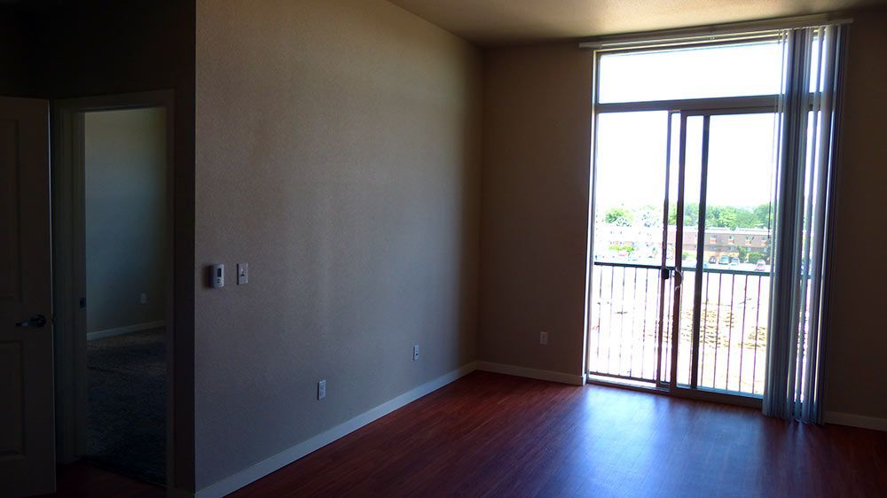 Empty room with dark wood floor, beige walls, and sliding glass door opening to a balcony.