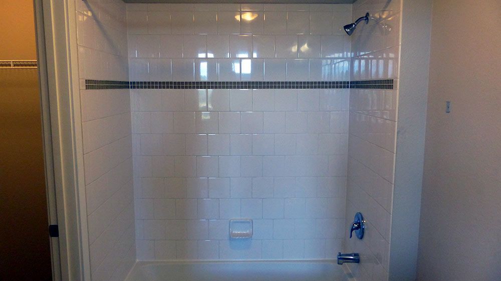 Bathroom shower with white tile walls, a black accent stripe, and a bathtub faucet