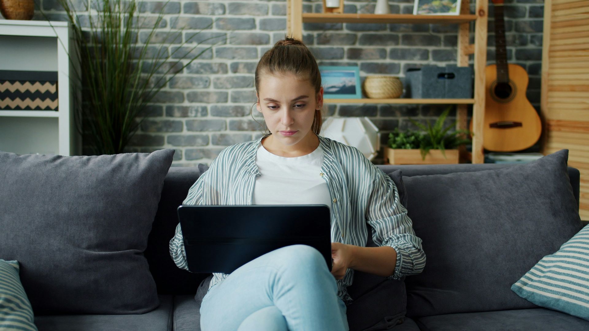 Woman using a laptop on a gray couch in a cozy living room.
