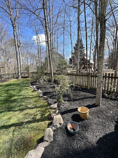A backyard with a fence , rocks , and potted plants.