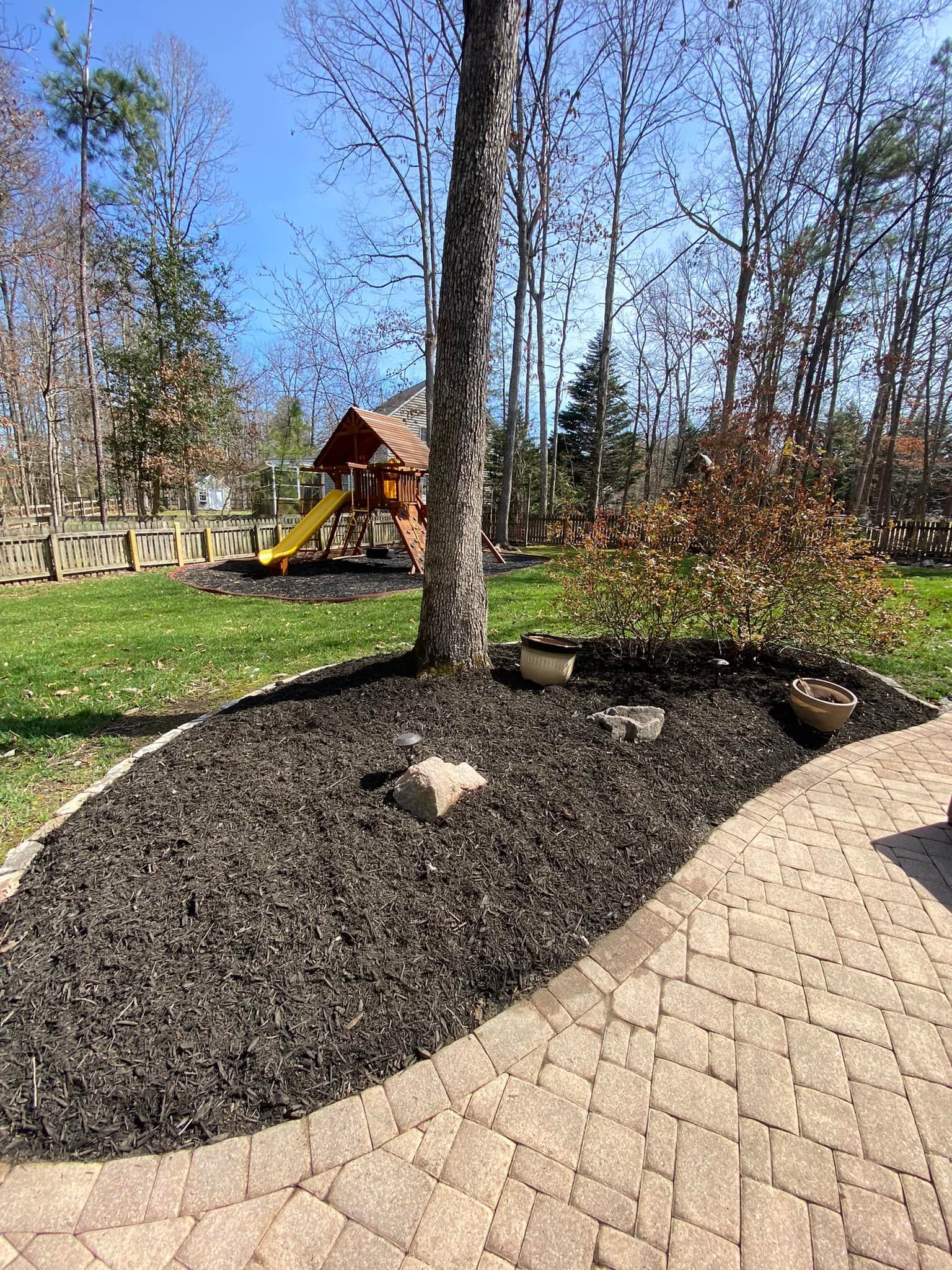 A brick walkway leading to a playground in a backyard.