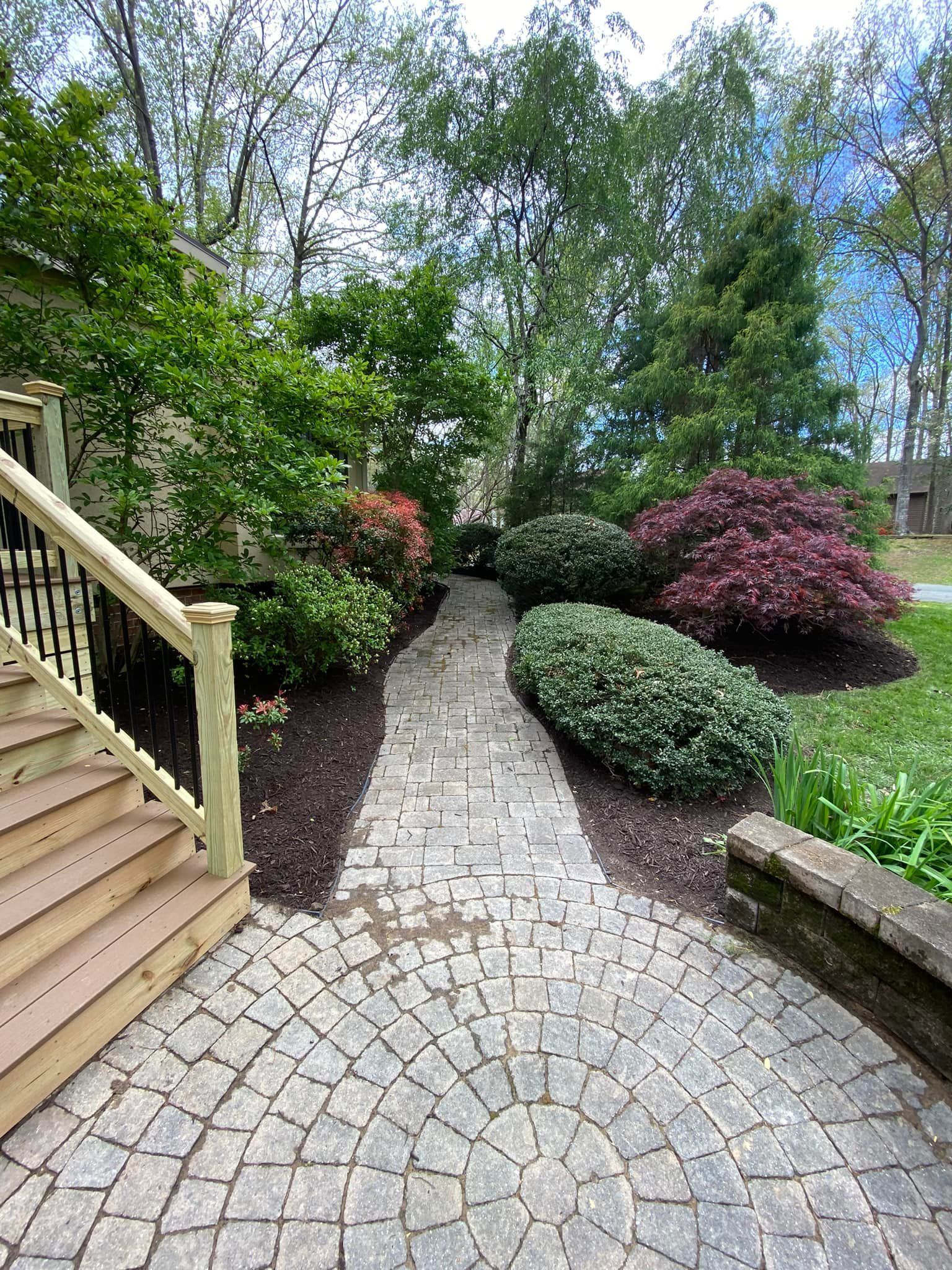 A brick walkway leading to a house with a wooden deck and stairs.