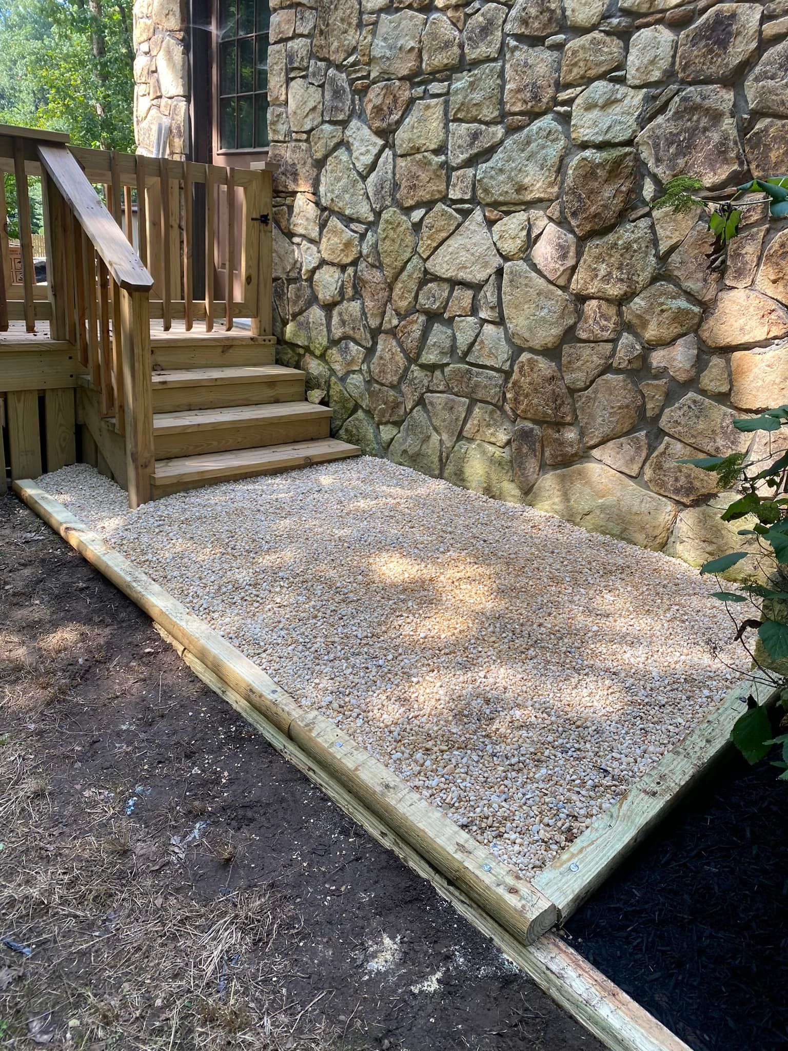 A wooden deck with stairs and gravel in front of a stone wall.