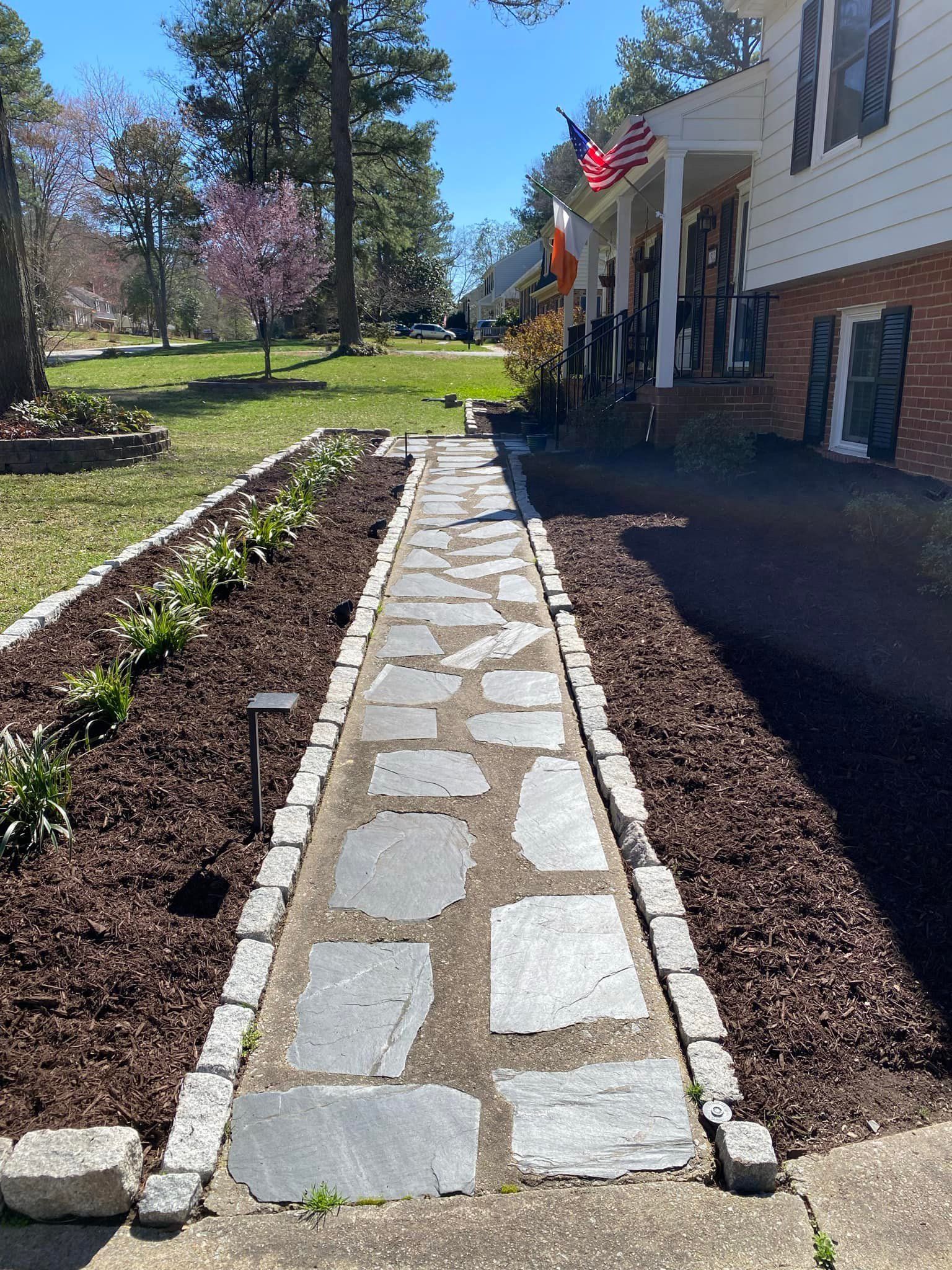 A stone walkway leading to a house with a flag on the porch.