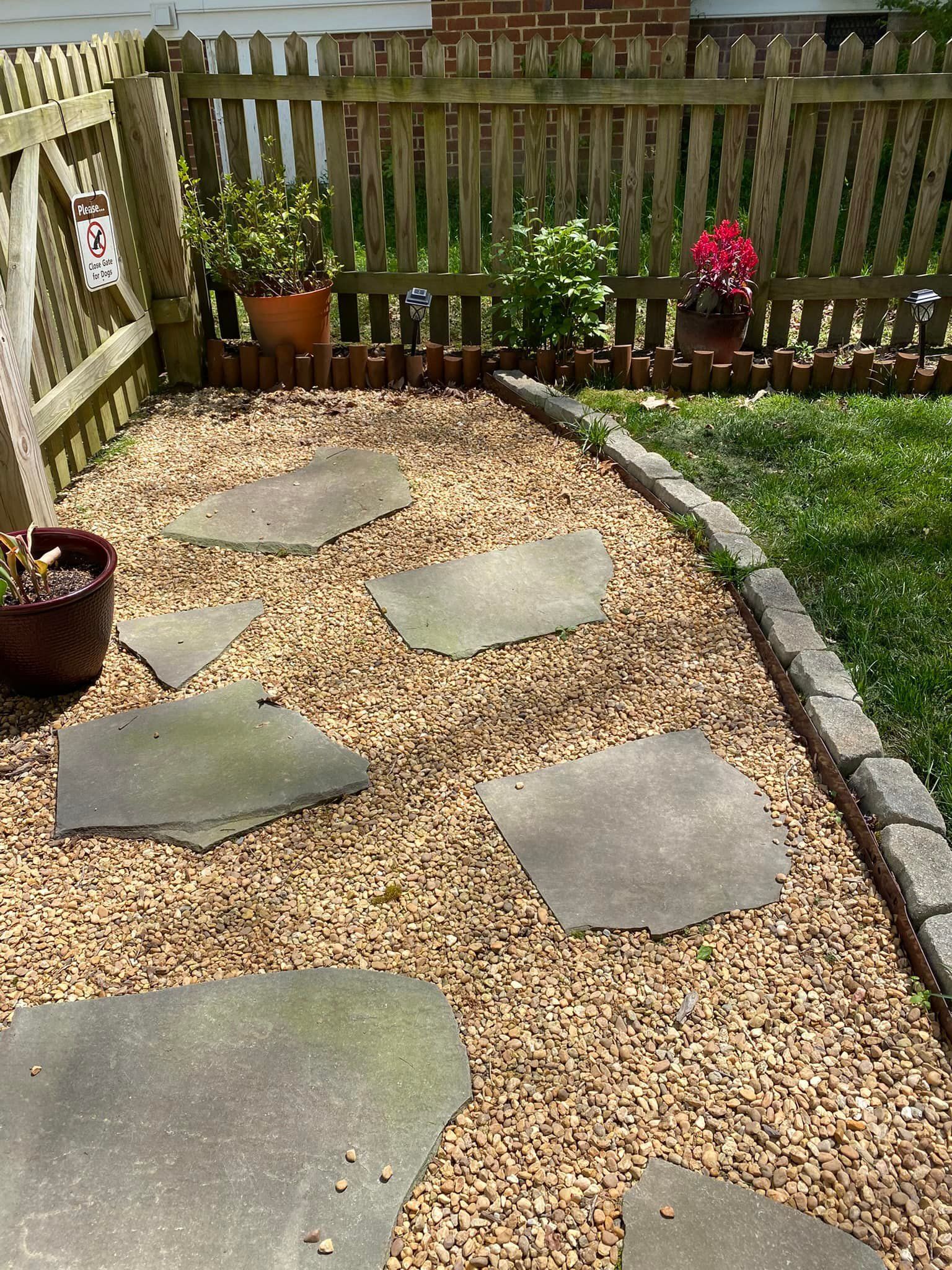 A stone walkway in a backyard next to a wooden fence.