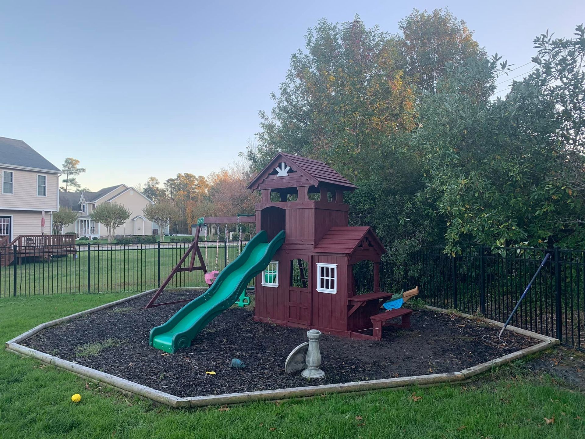 A red playhouse with a green slide and swings in a backyard.