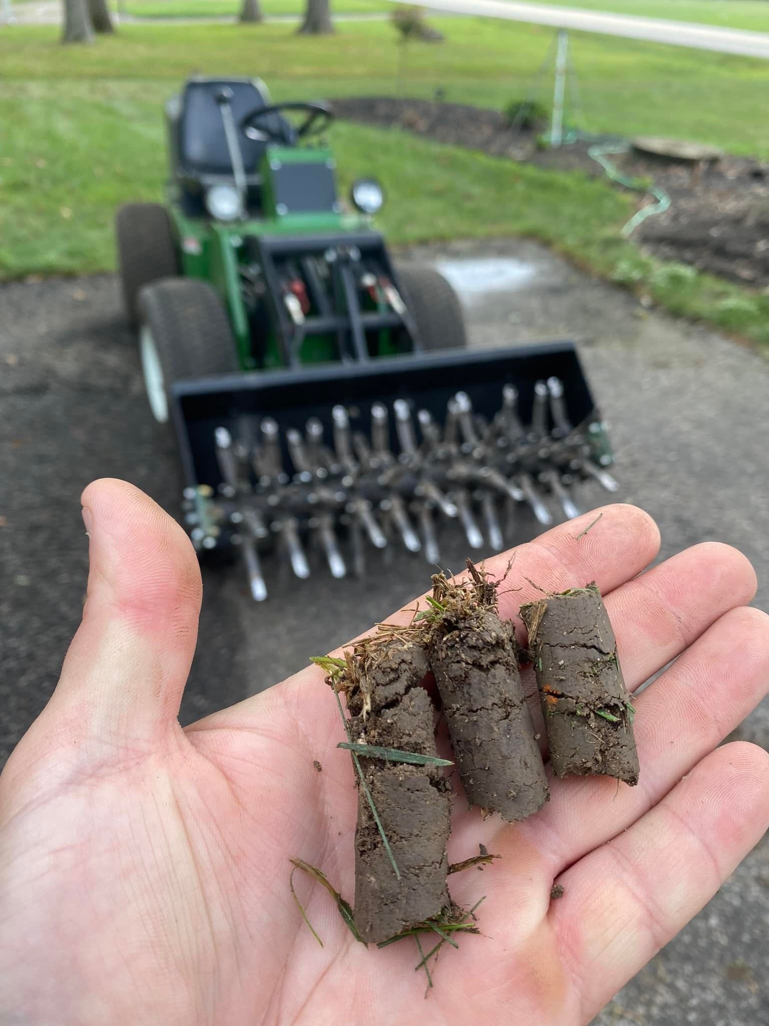 A person is holding a handful of dirt in front of a lawn mower.