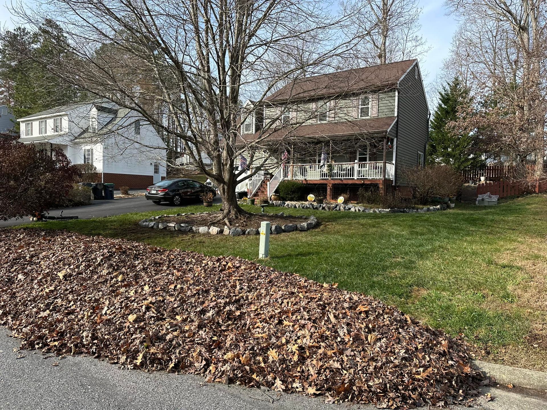 A pile of leaves is on the side of the road in front of a house.