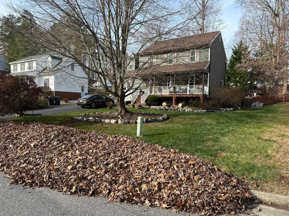 There is a pile of leaves on the side of the road in front of a house.