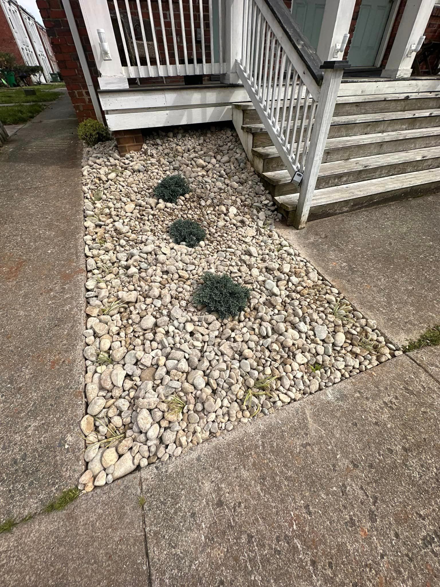 There is a rock garden in front of a house with stairs.