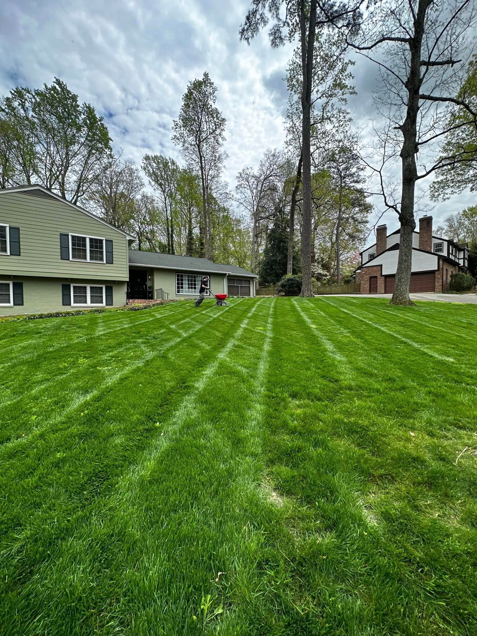 A lush green lawn in front of a house with trees in the background.