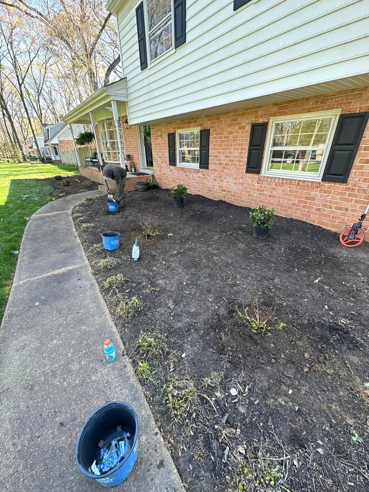 A man is planting flowers in front of a brick house.