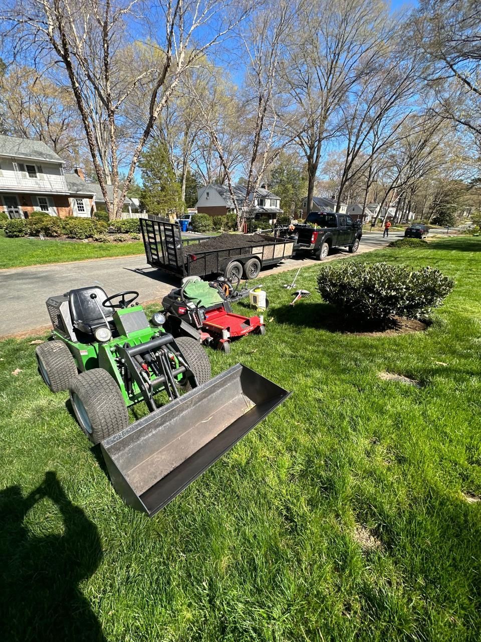 A green lawn mower is parked in the grass next to a truck.