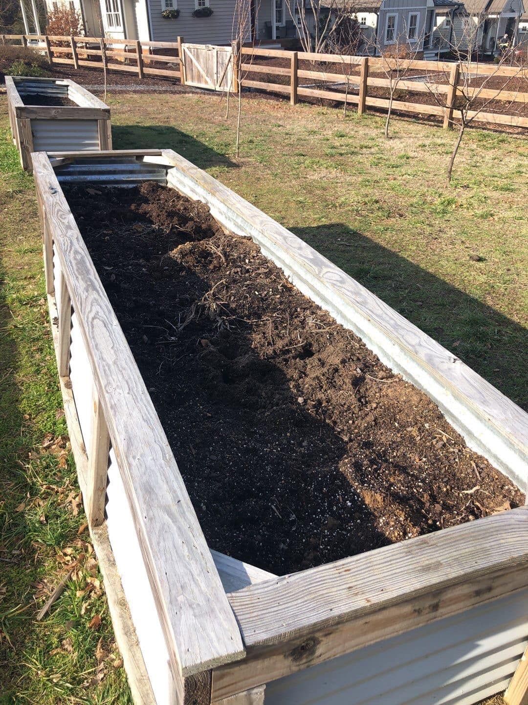 A wooden planter filled with dirt and a fence in the background